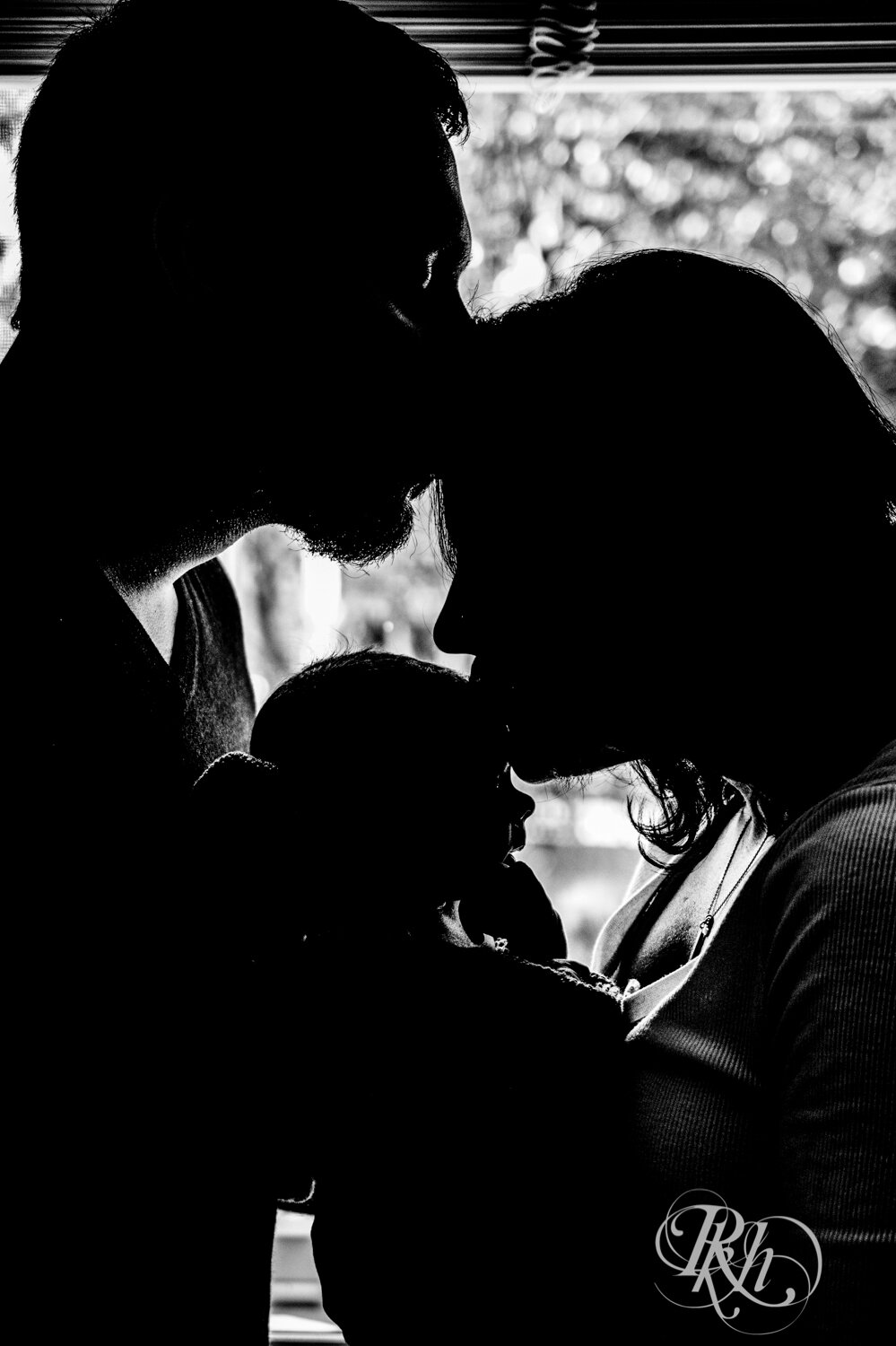 Mom and dad kiss in silhouette with baby between them in Minnesota.