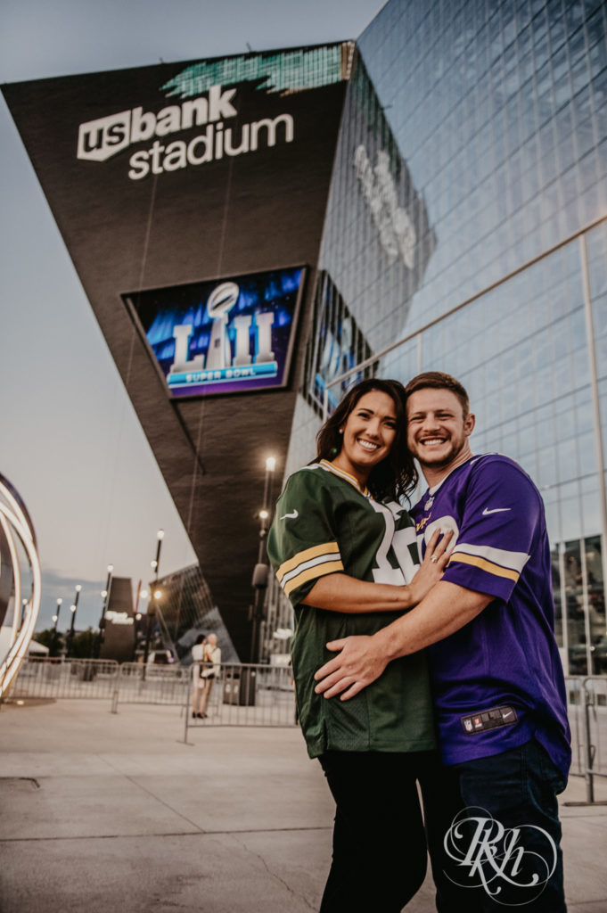 Man in Vikings jersey and woman in Packers jersey stand in front of the US Bank Stadium in Minneapolis, Minnesota.