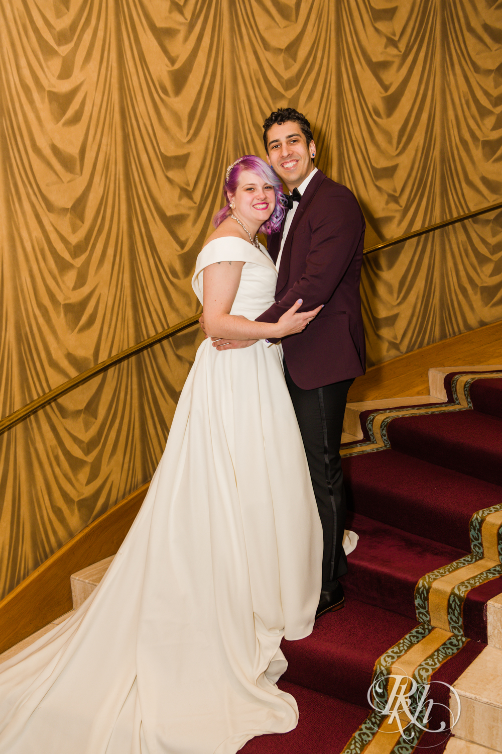Bride with rainbow hair and groom in maroon suit smile at the Saint Paul Hotel in Saint Paul, Minnesota.