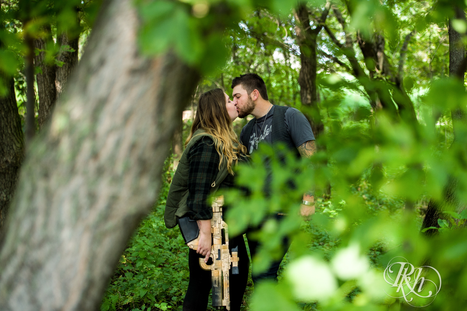Man with XBox gun and woman with Harry Potter wand kiss during engagement session in woods in Plymouth, Minnesota.