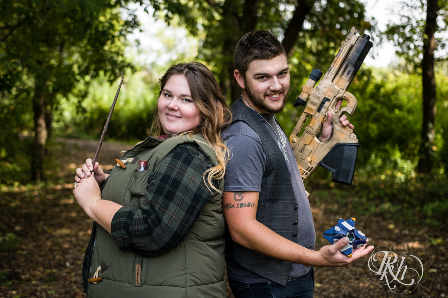 Man with XBox gun and woman with Harry Potter wand smile during engagement session in woods in Plymouth, Minnesota.