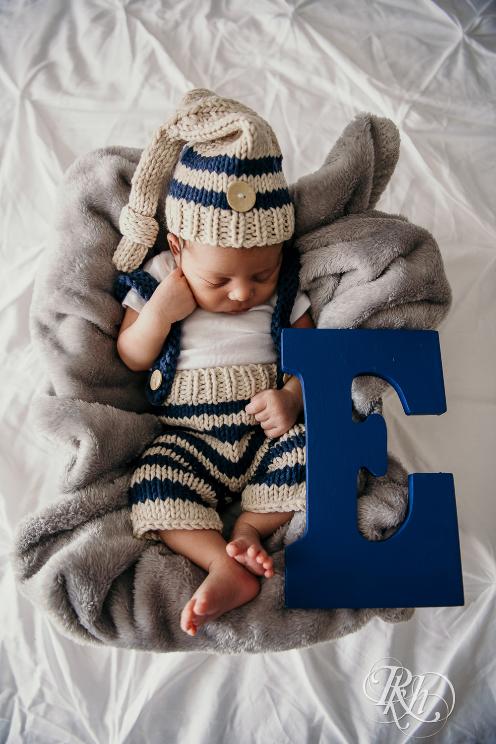 Biracial baby wearing knit cap sleeps on a bed in Burnsville, Minnesota at home with big letter E.