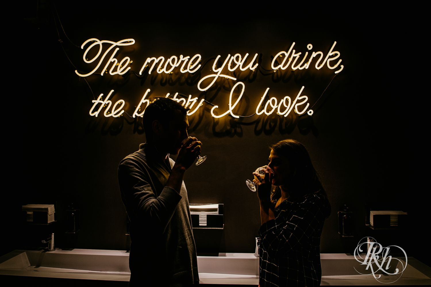 Man and woman in flannel and jeans drink in front of neon sign at Headflyer Brewery in Minneapolis, Minnesota.