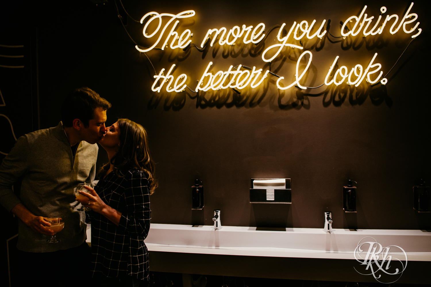 Man and woman in flannel and jeans kiss in front of neon sign at Headflyer Brewery in Minneapolis, Minnesota.
