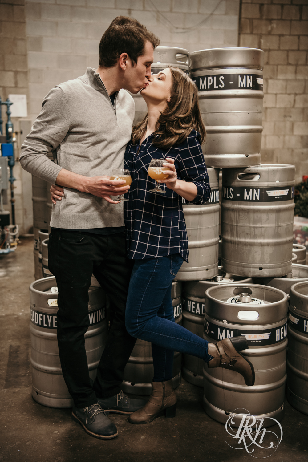 Man and woman in flannel and jeans kiss in front of barrels at Headflyer Brewery in Minneapolis, Minnesota.