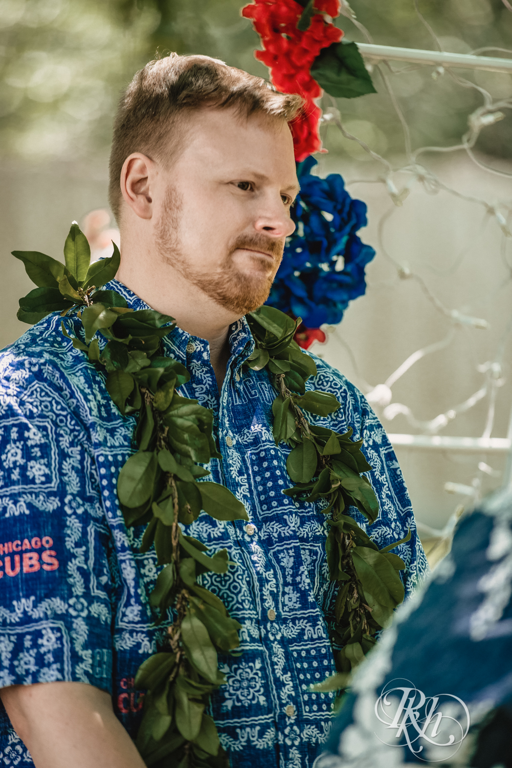 Two grooms hold hands during backyard elopement ceremony while wearing Hawaiian shirts and leis.