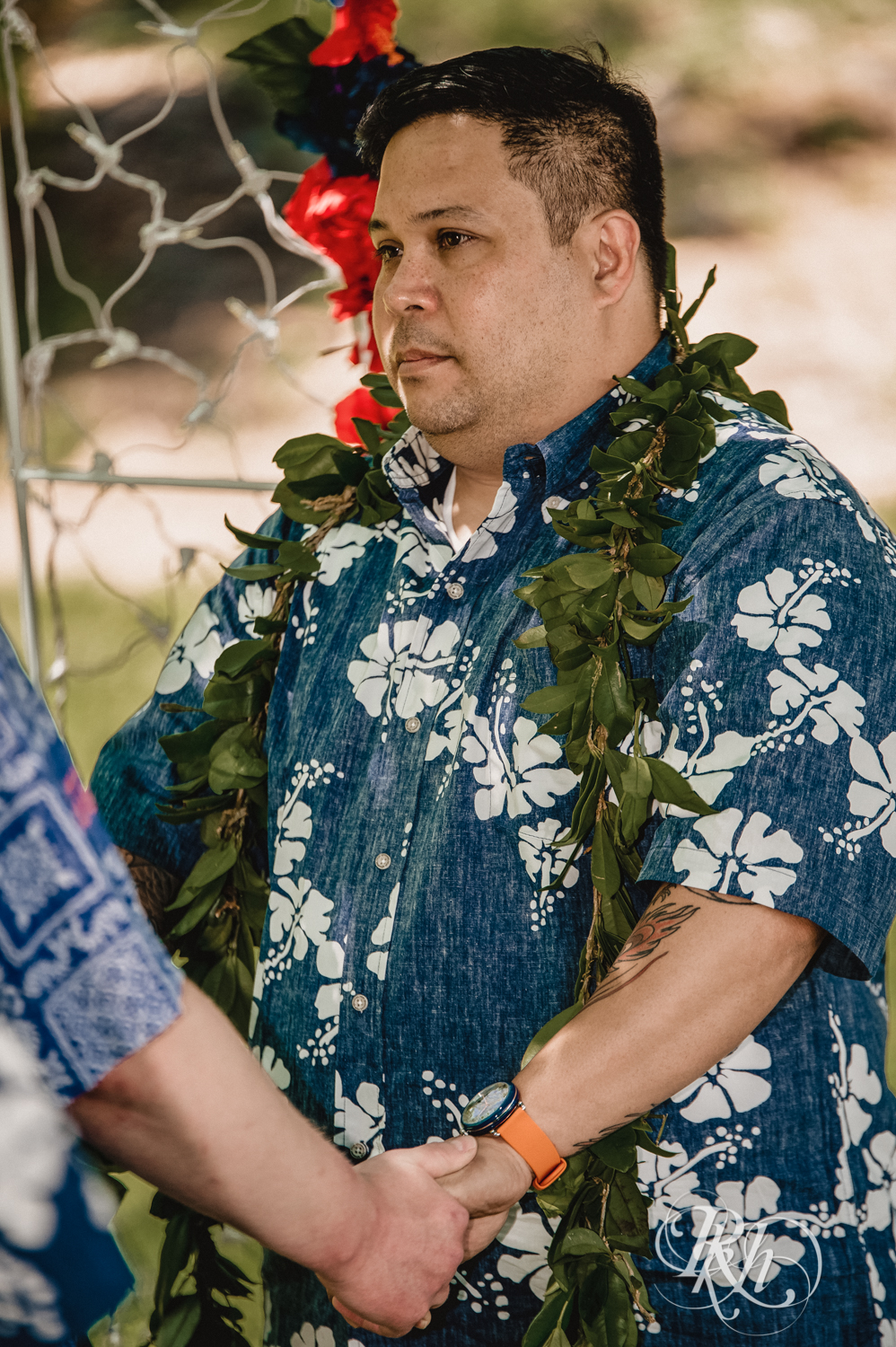 Two grooms hold hands during backyard elopement ceremony while wearing Hawaiian shirts and leis.