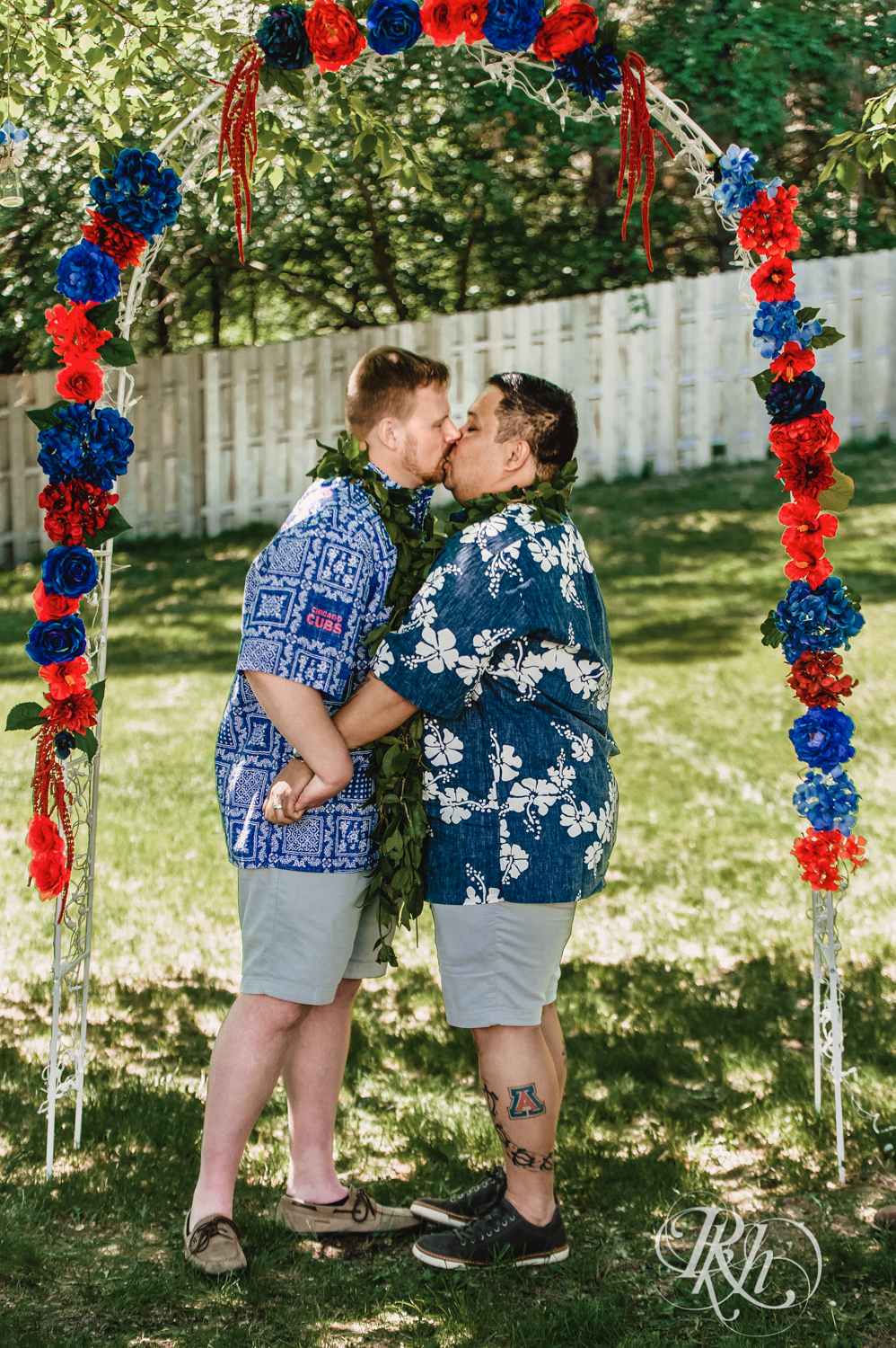 Two grooms kiss during backyard elopement ceremony while wearing Hawaiian shirts and leis.
