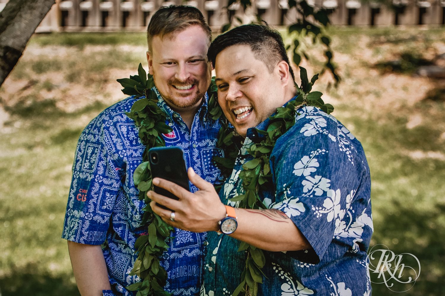 Two grooms talk to wedding guests on Zoom while wearing Hawaiian shirts and leis.