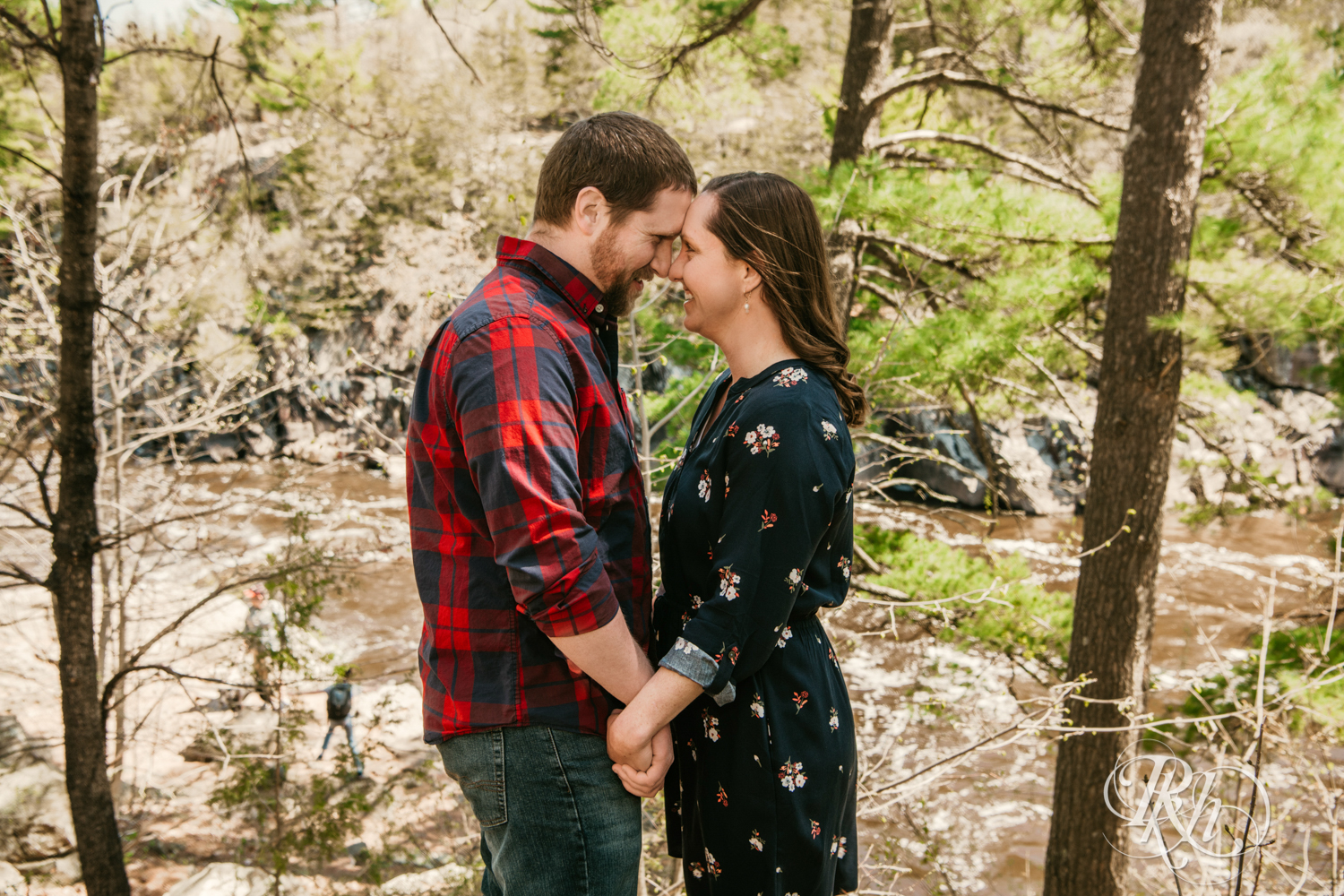 Man in flannel and jeans and woman in dress smile on cliff over river in Taylor's Falls, Minnesota.