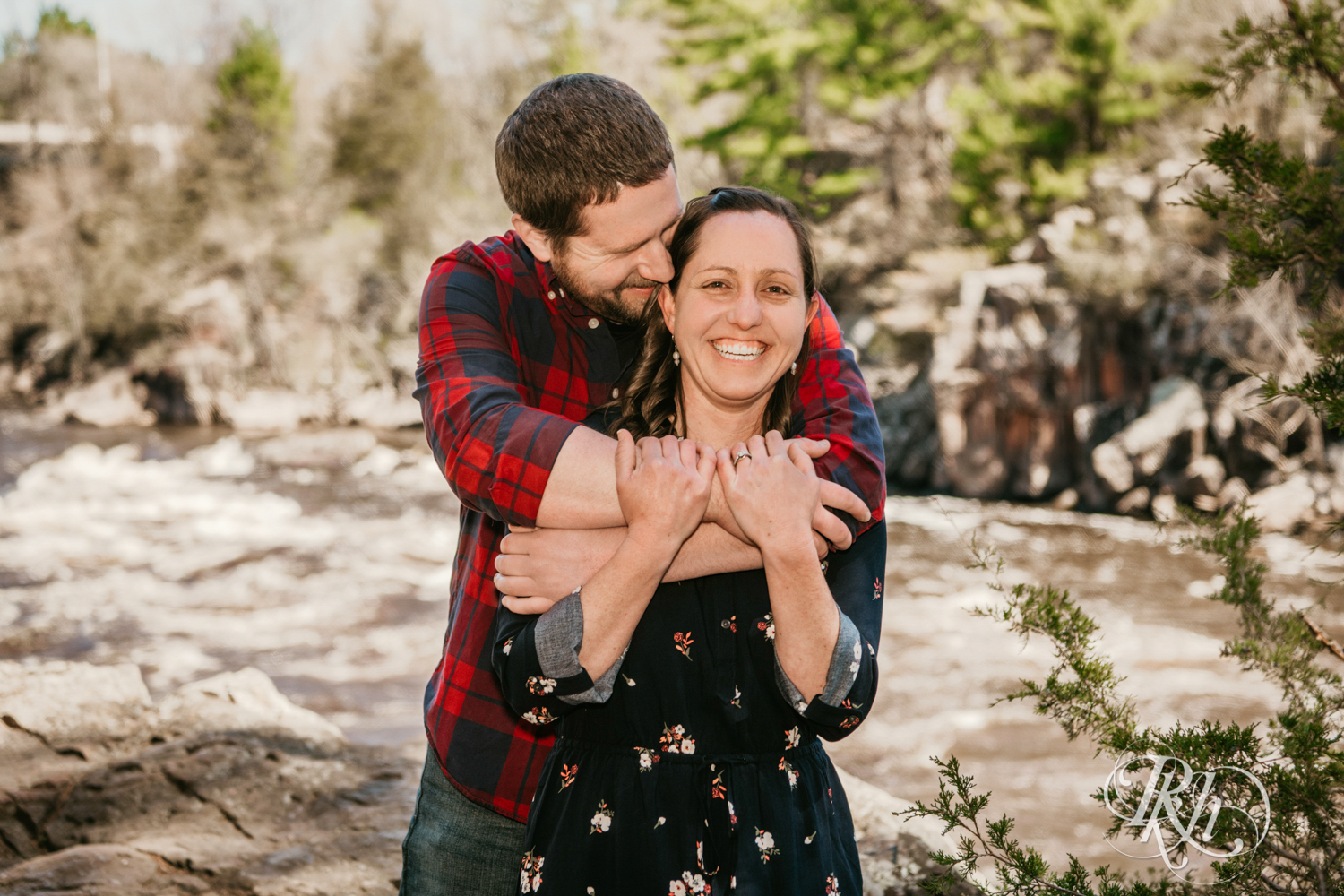 Man in flannel and jeans and woman in dress smile on cliff over river in Taylor's Falls, Minnesota.