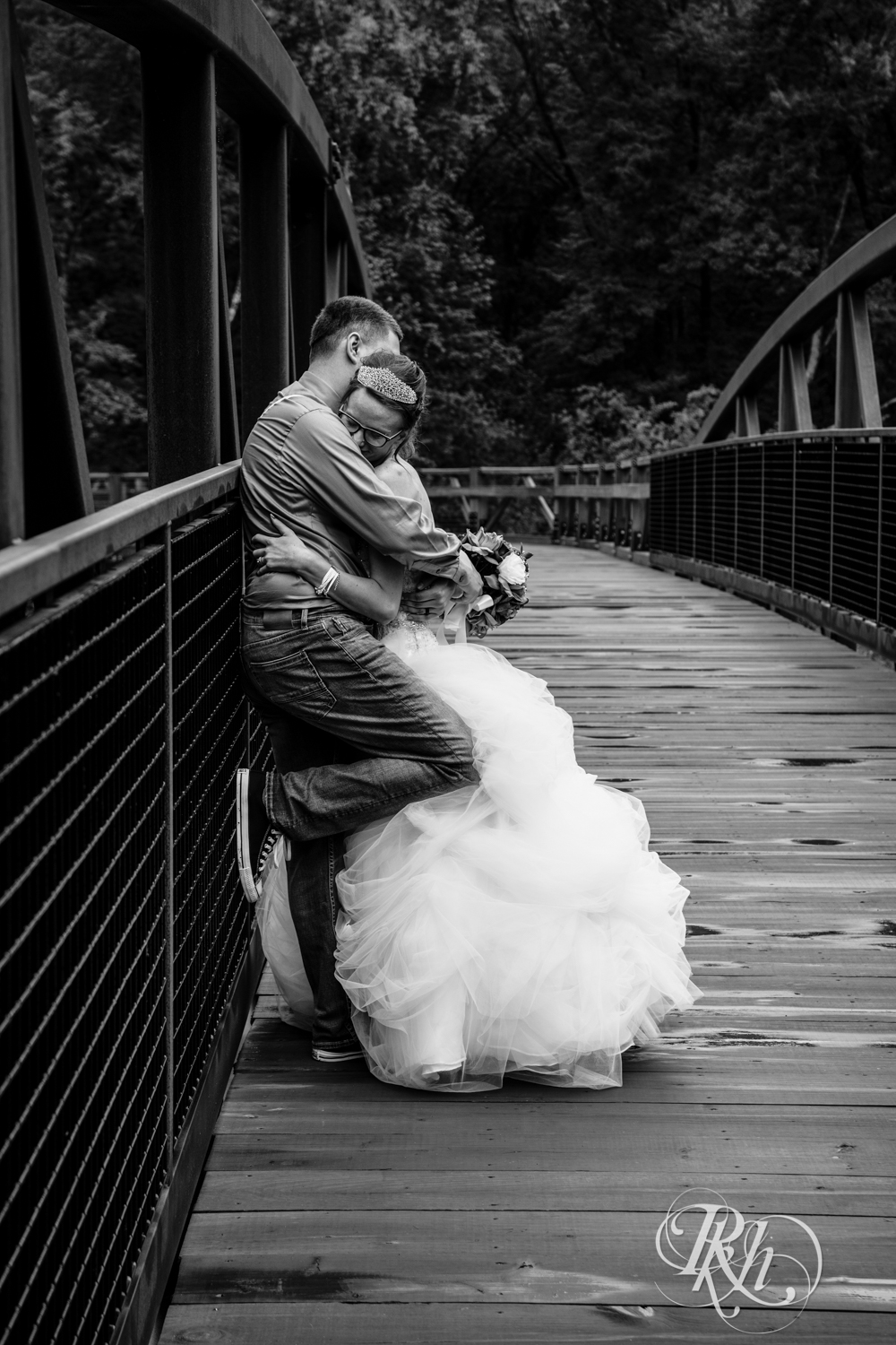 Bride and groom hug on a bridge in the rain in Irvine Park in Chippewa Falls, Wisconsin. 