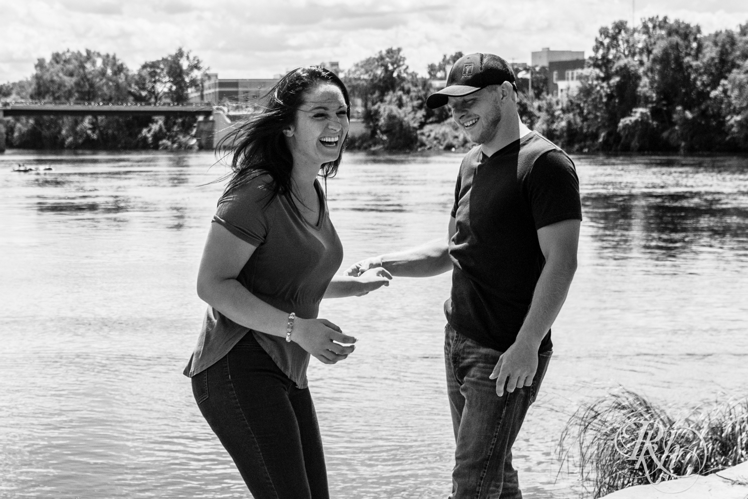 Man and woman laugh in front of a lake in Phoenix Park in Eau Claire, Wisconsin on a sunny day. 
