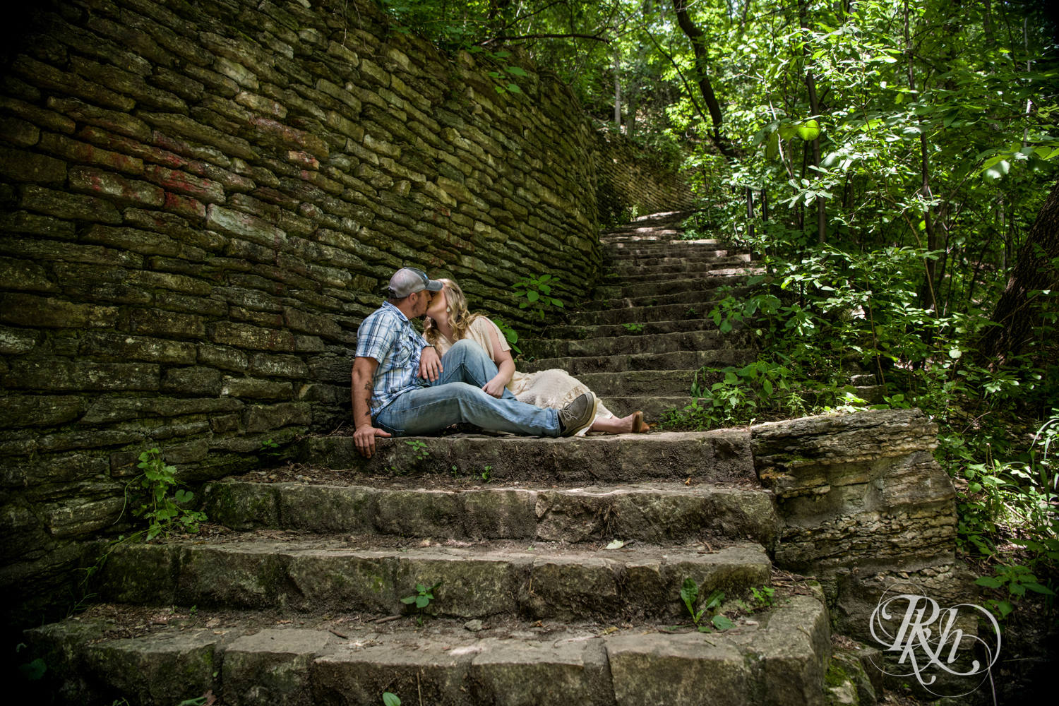 Man in jeans and woman in yellow dress kissing on outdoor stairs in Hidden Falls Regional Park in Saint Paul, Minnesota.