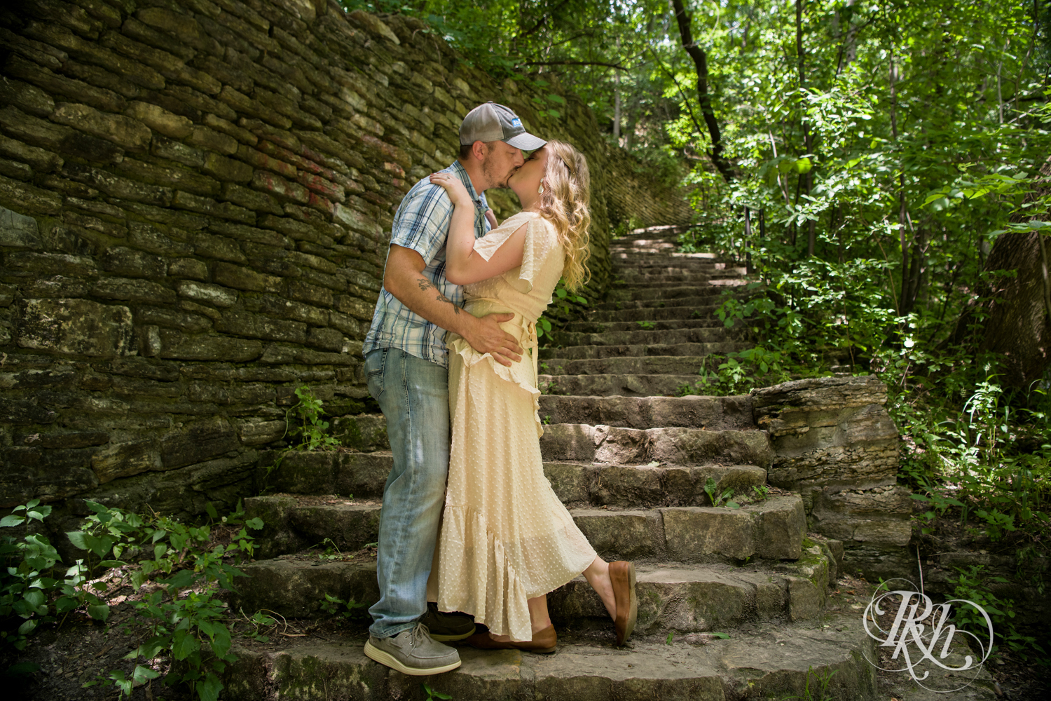 Man in jeans and woman in yellow dress kissing on outdoor stairs in Hidden Falls Regional Park in Saint Paul, Minnesota.