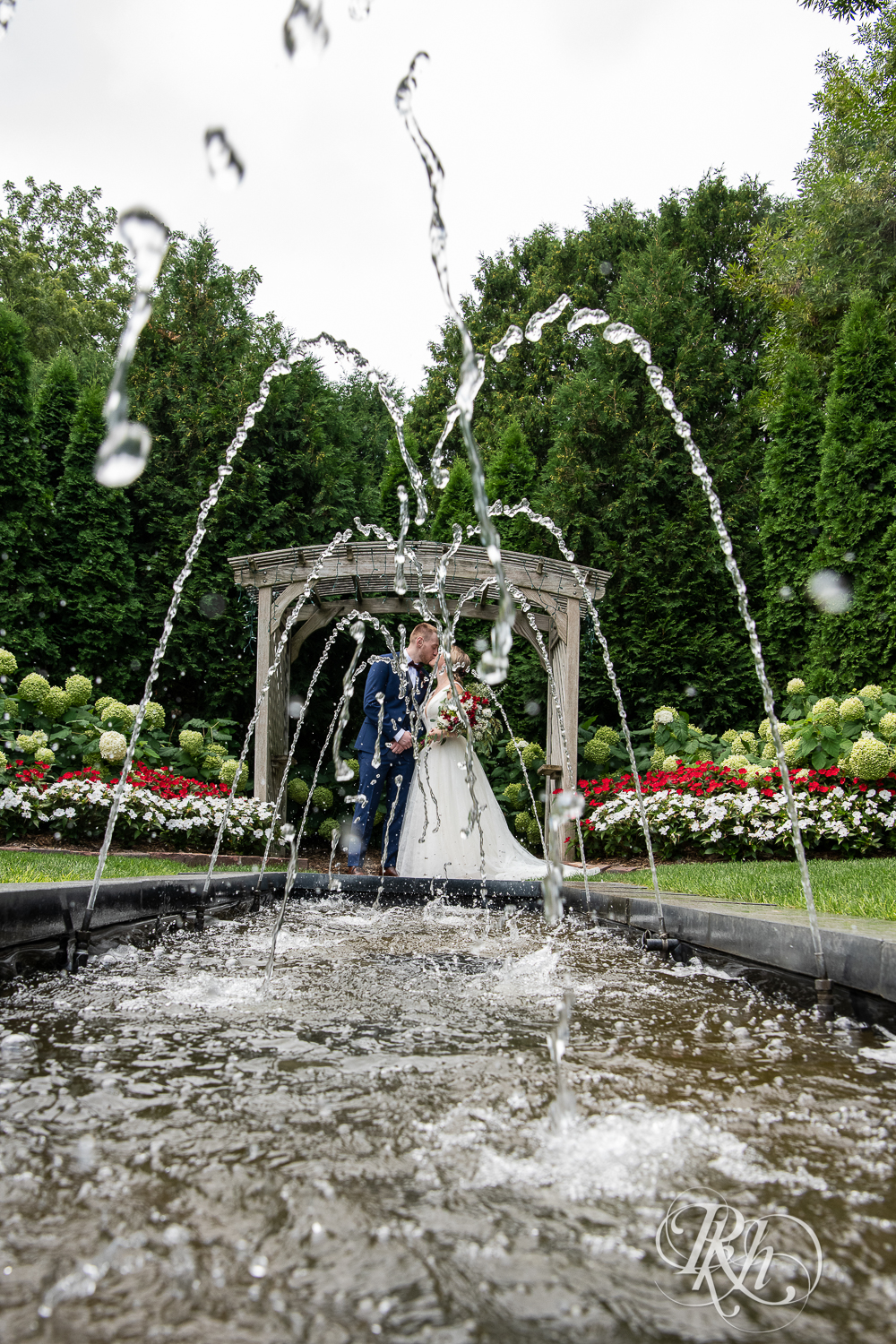 Bride and groom kiss behind fountain at the William Sauntry Mansion in Stillwater, Minnesota.