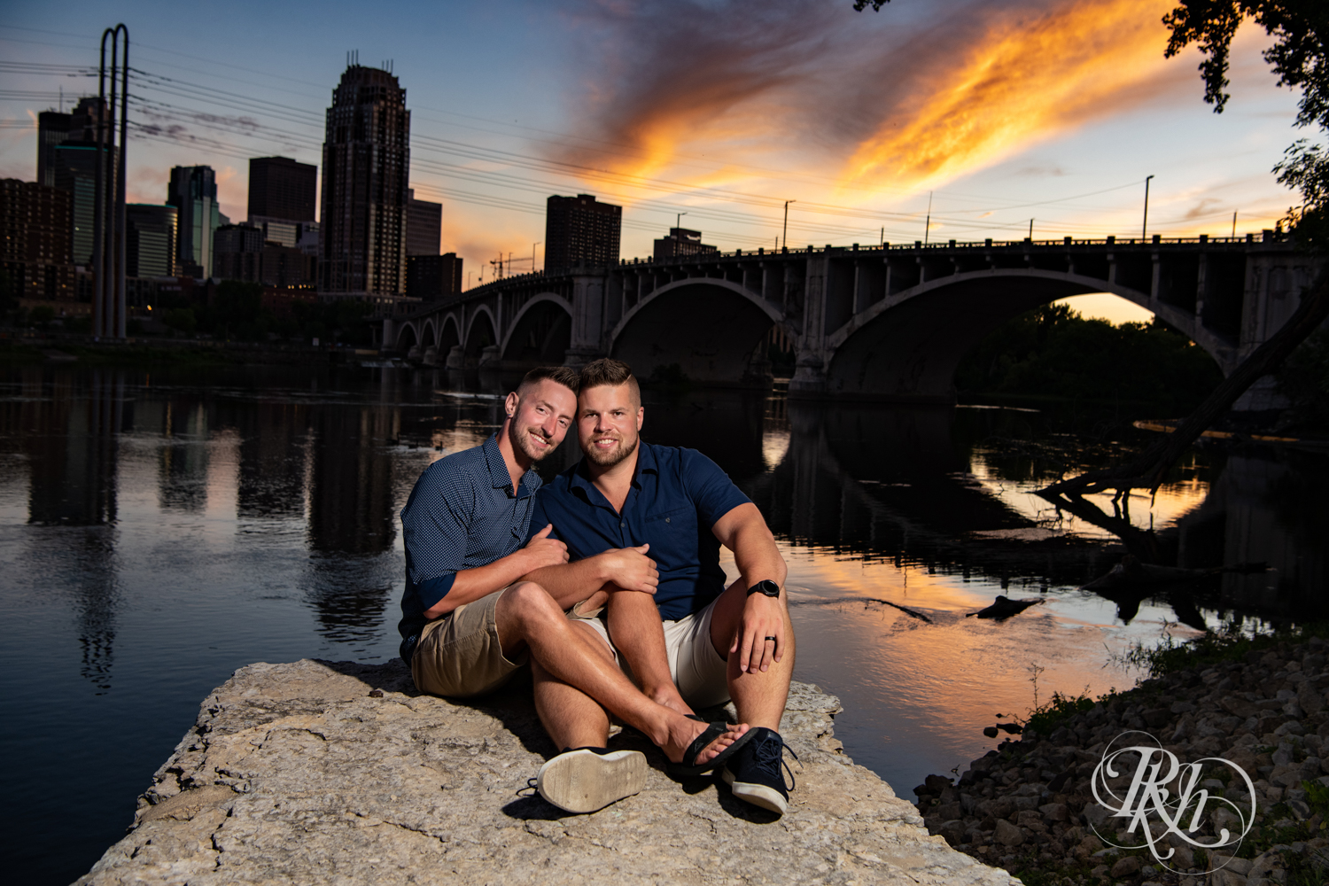 Two gay men snuggle in front of river during sunset in Saint Anthony Main in Minneapolis, Minnesota.