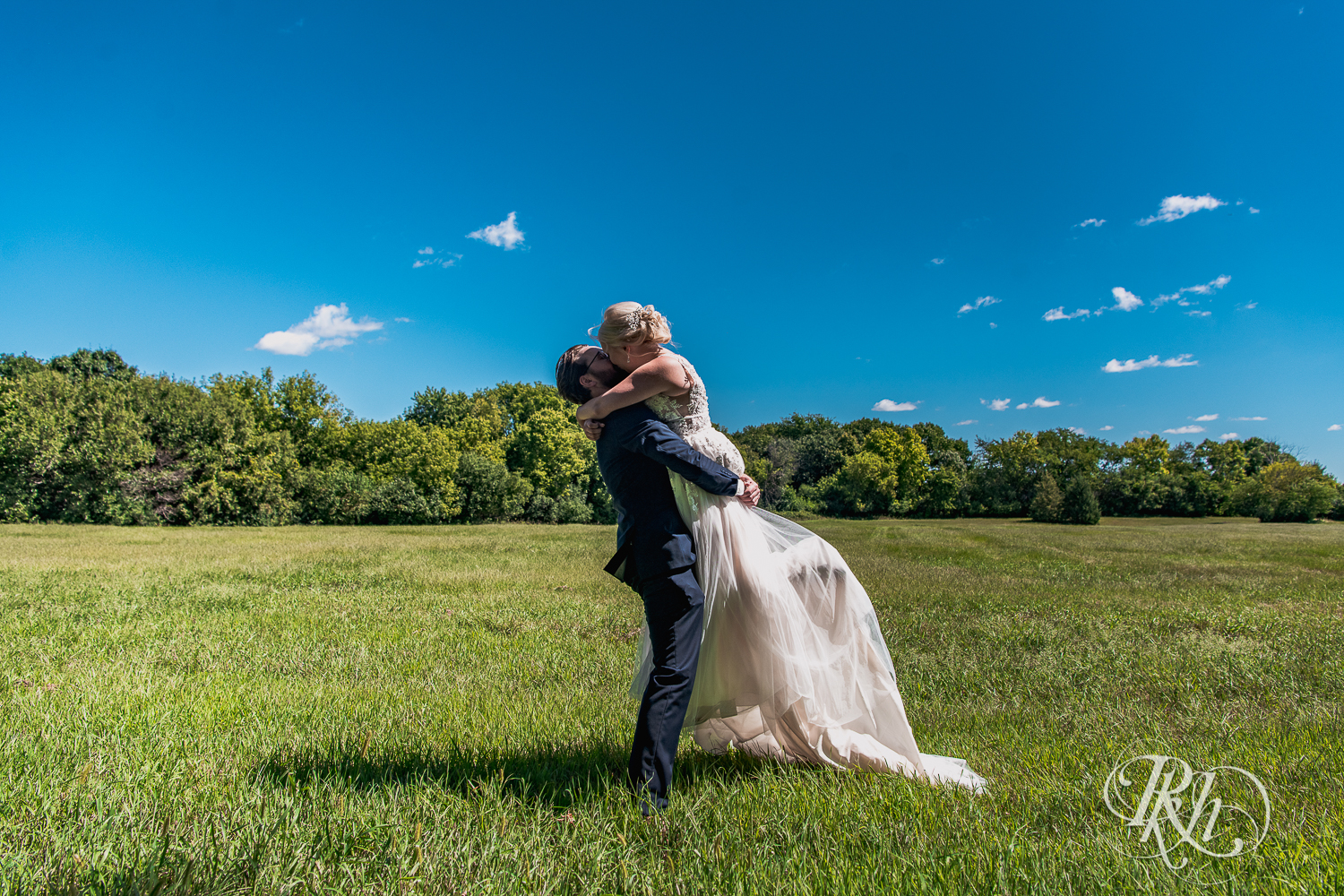 Groom lifts and kisses bride in sunny field at Green Acres Event Center in Eden Prairie, Minnesota.