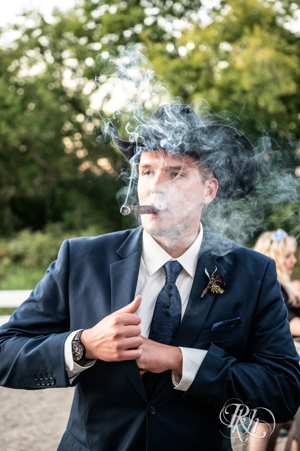 Groomsman in cowboy hat smokes cigar at Green Acres Event Center in Eden Prairie, Minnesota.