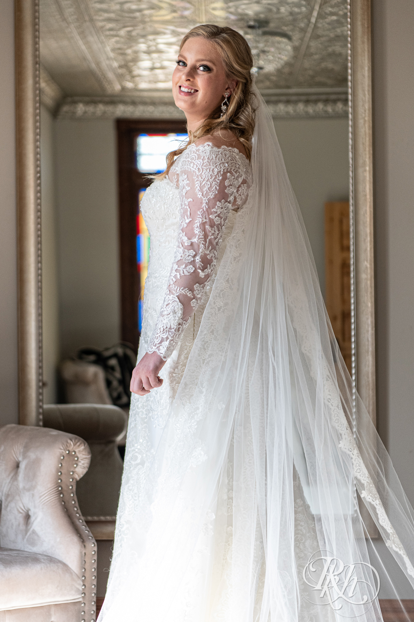 Bride standing in front of mirror in long sleeve wedding dress and cathedral veil at Weddings at the Broz in New Prague, Minnesota.