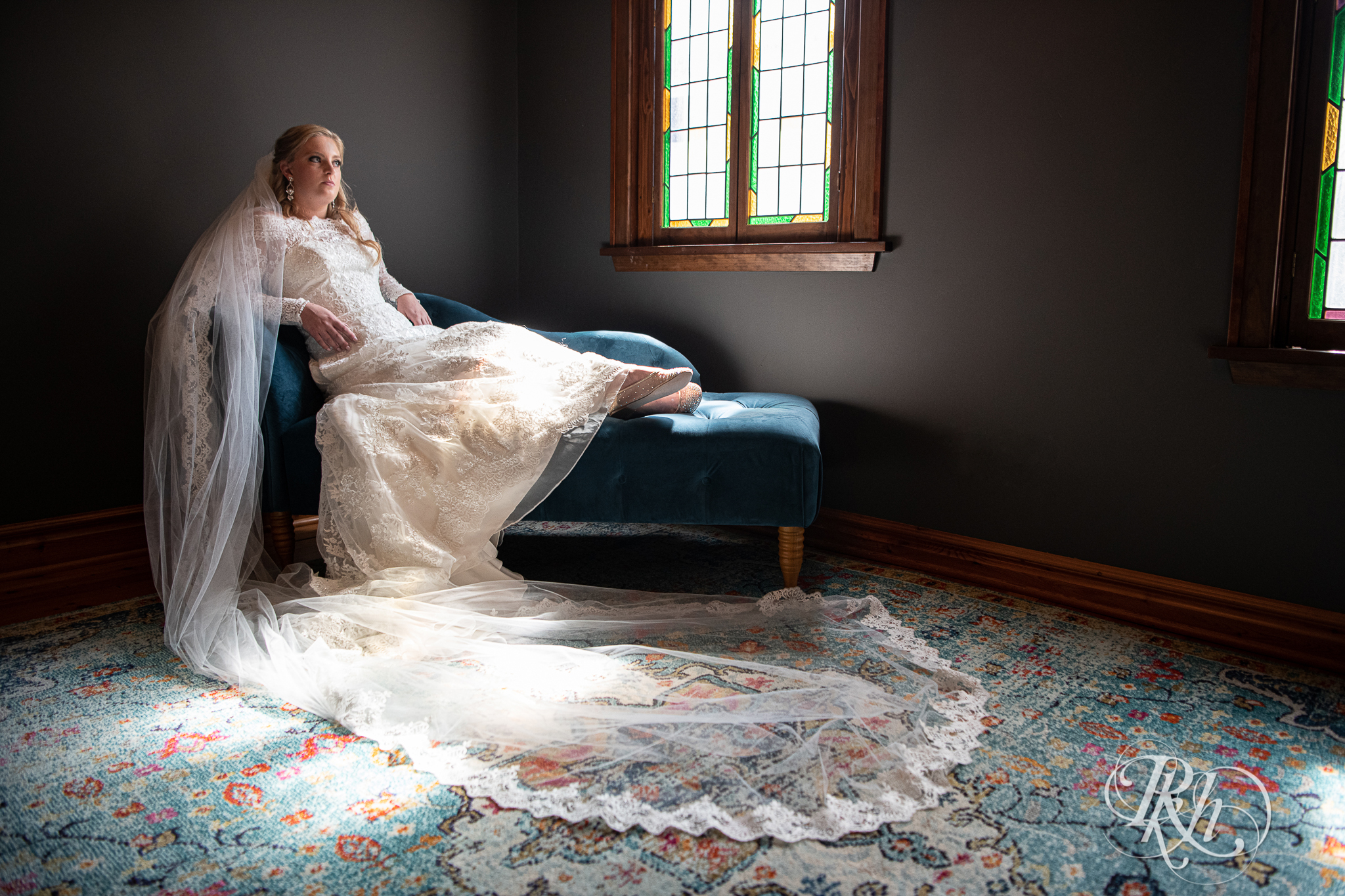 Bride sitting on couch in long sleeve wedding dress and cathedral veil at Weddings at the Broz in New Prague, Minnesota.