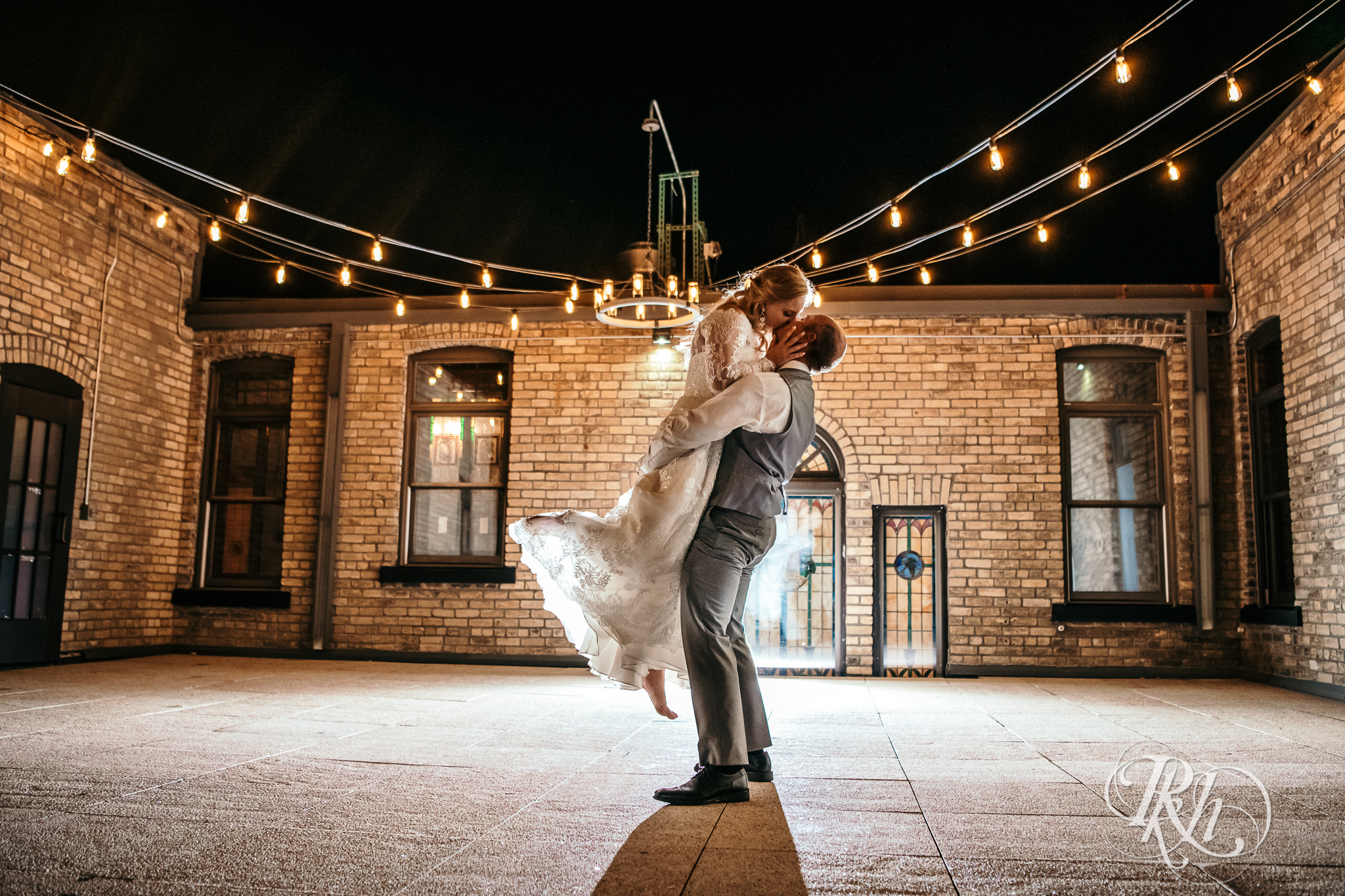 Groom lifts and kisses bride under lights at night at Weddings at the Broz in New Prague, Minnesota.