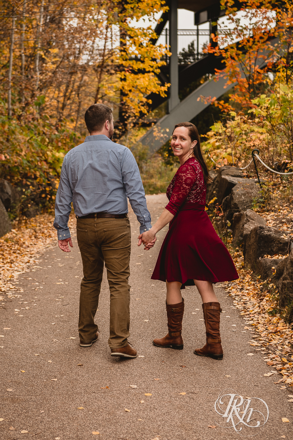 Man and woman in red dress walk together in front of the fall colors in Gooseberry Falls in Two Harbors, Minnesota.