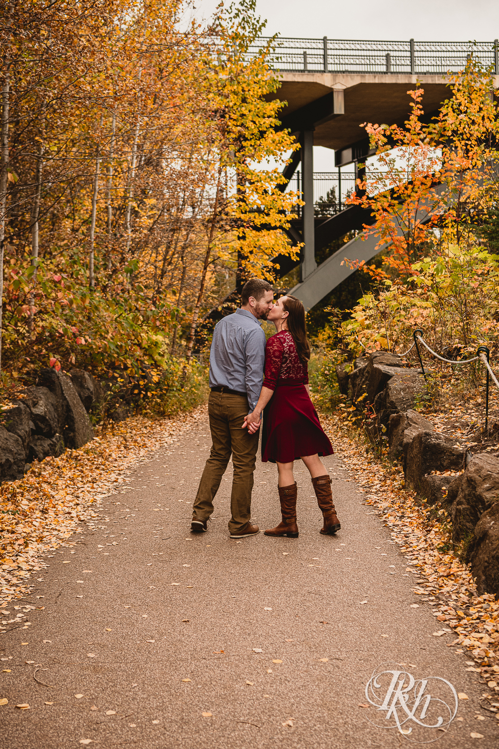 Man and woman in red dress kiss in front of the fall colors in Gooseberry Falls in Two Harbors, Minnesota.