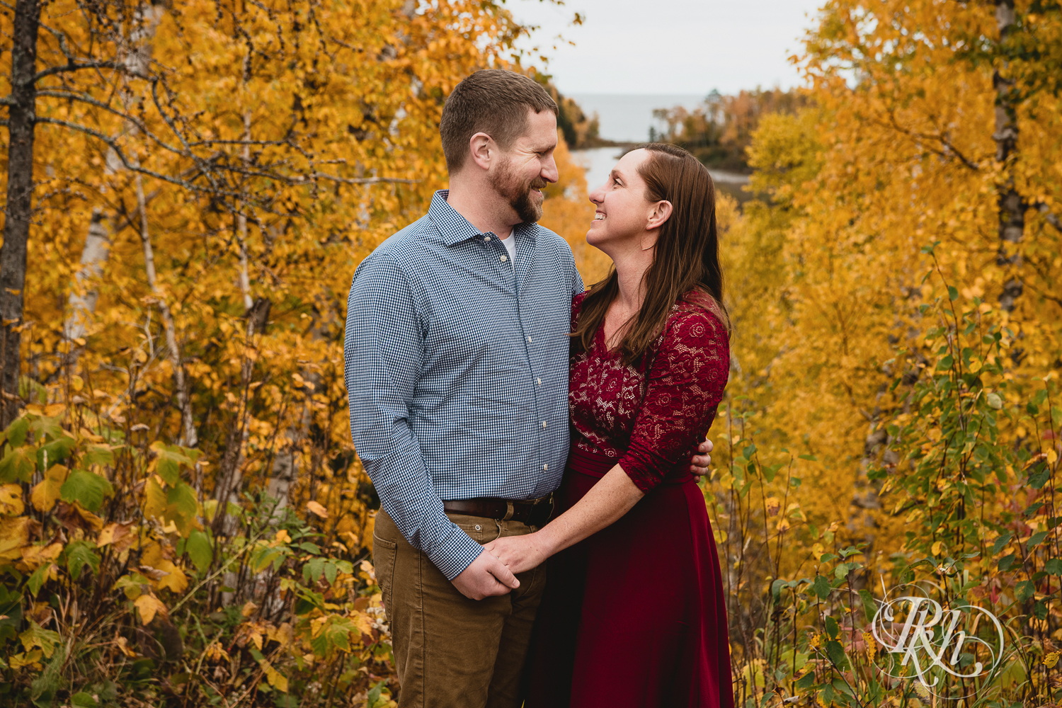 Man and woman in red dress smile in front of fall colors in Gooseberry Falls in Two Harbors, Minnesota.