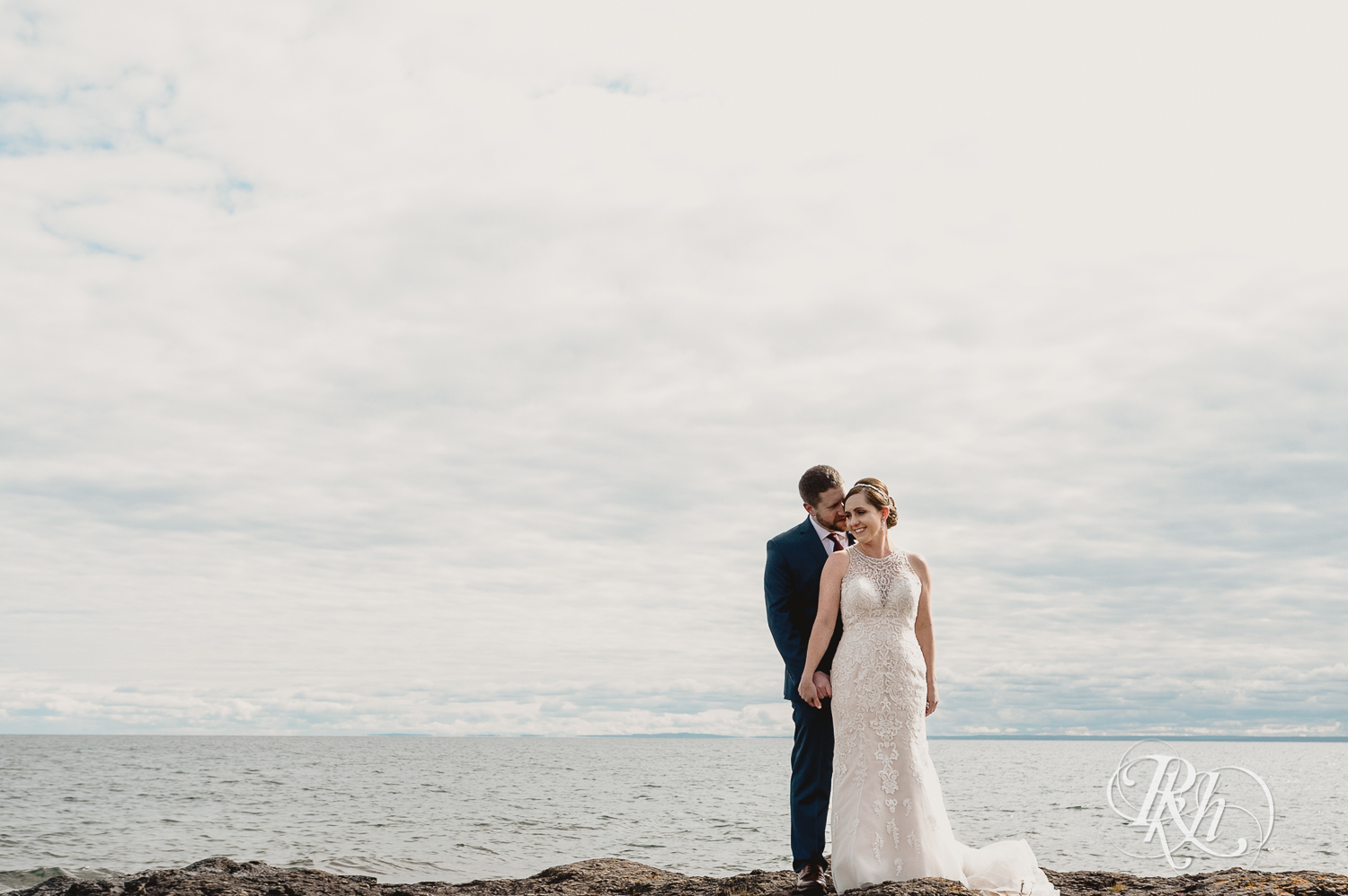 Bride and groom smile on rock in front of Lake Superior at Superior Shores Resort in Two Harbors, Minnesota.