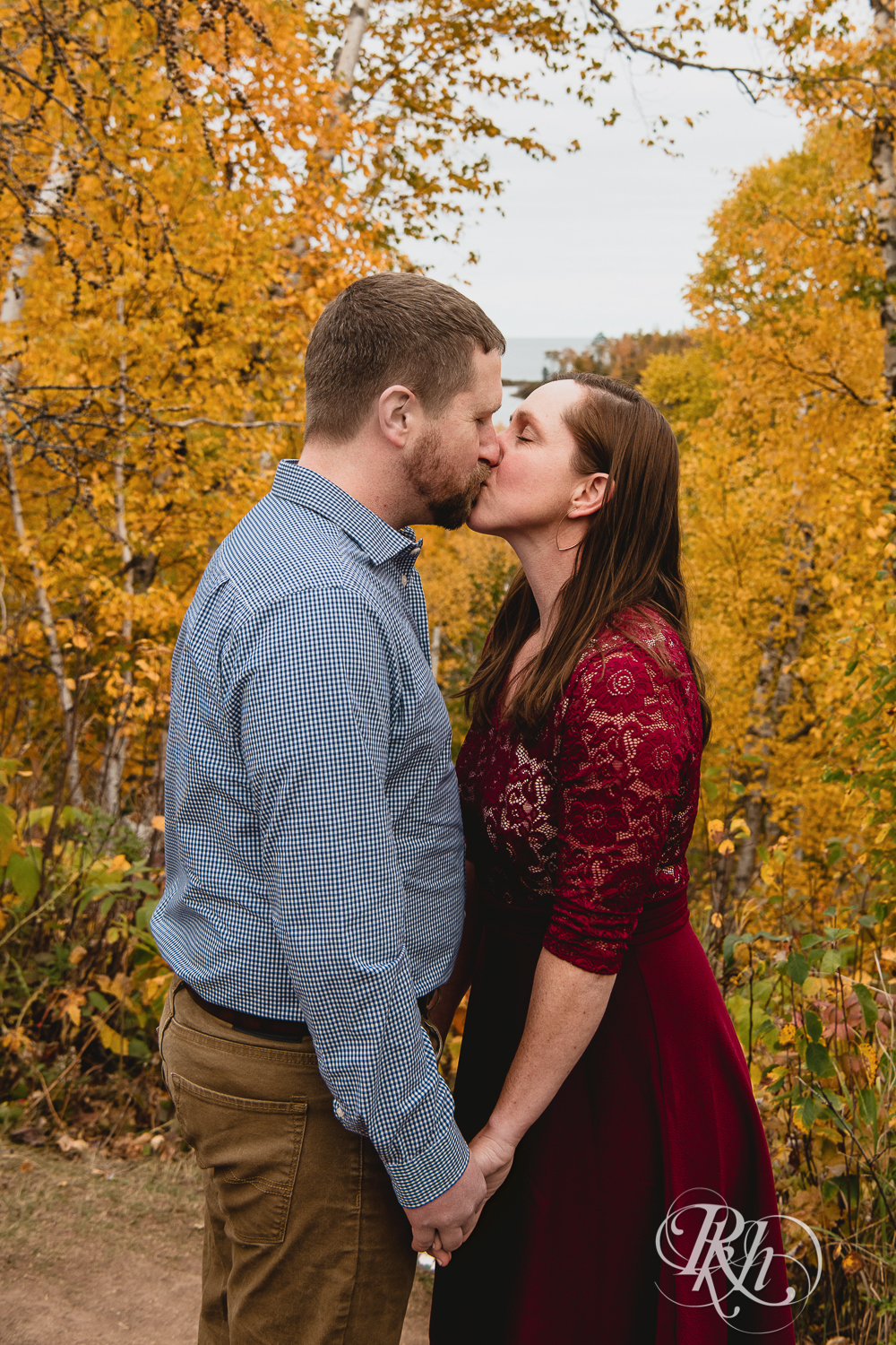 Man and woman in red dress kiss in front of fall colors in Gooseberry Falls in Two Harbors, Minnesota.