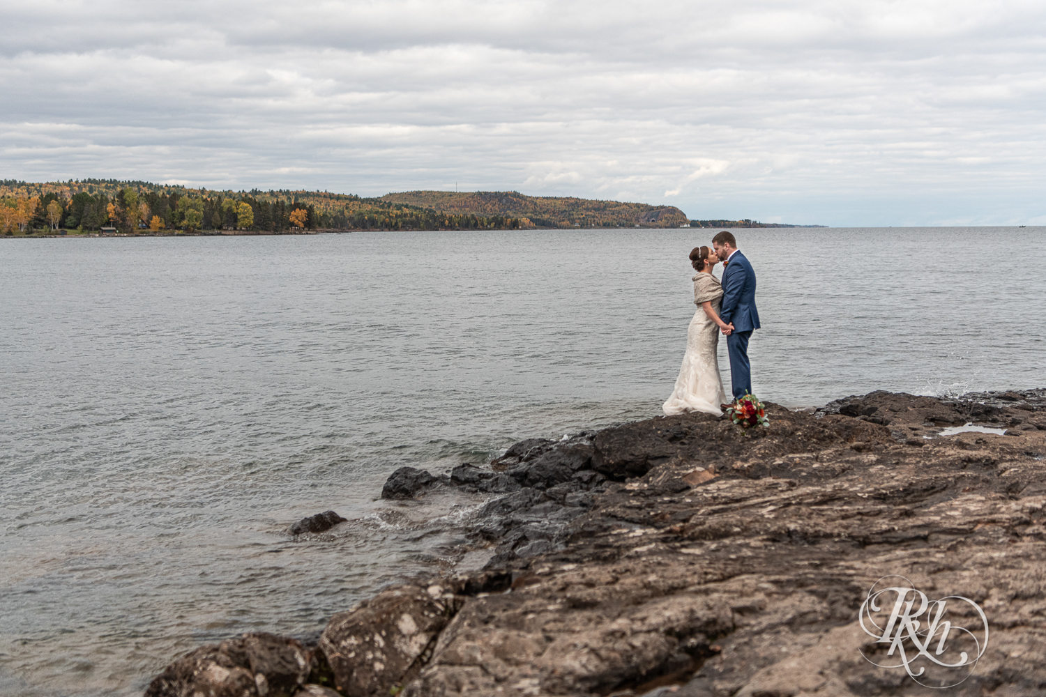 Bride and groom kiss on rock in Lake Superior at Superior Shores Resort in Two Harbors, Minnesota.