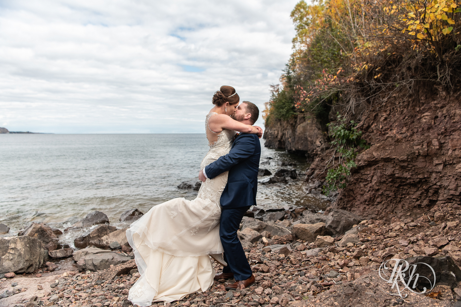 Groom lifts and kisses bride on rock in Lake Superior at Superior Shores Resort in Two Harbors, Minnesota.