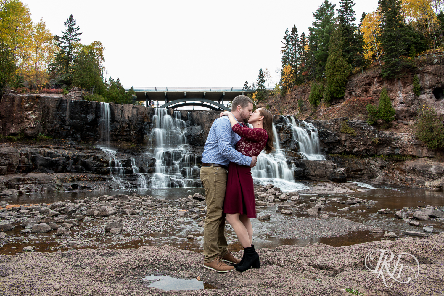 Man and woman in red dress kiss in front of the waterfall in Gooseberry Falls in Two Harbors, Minnesota.