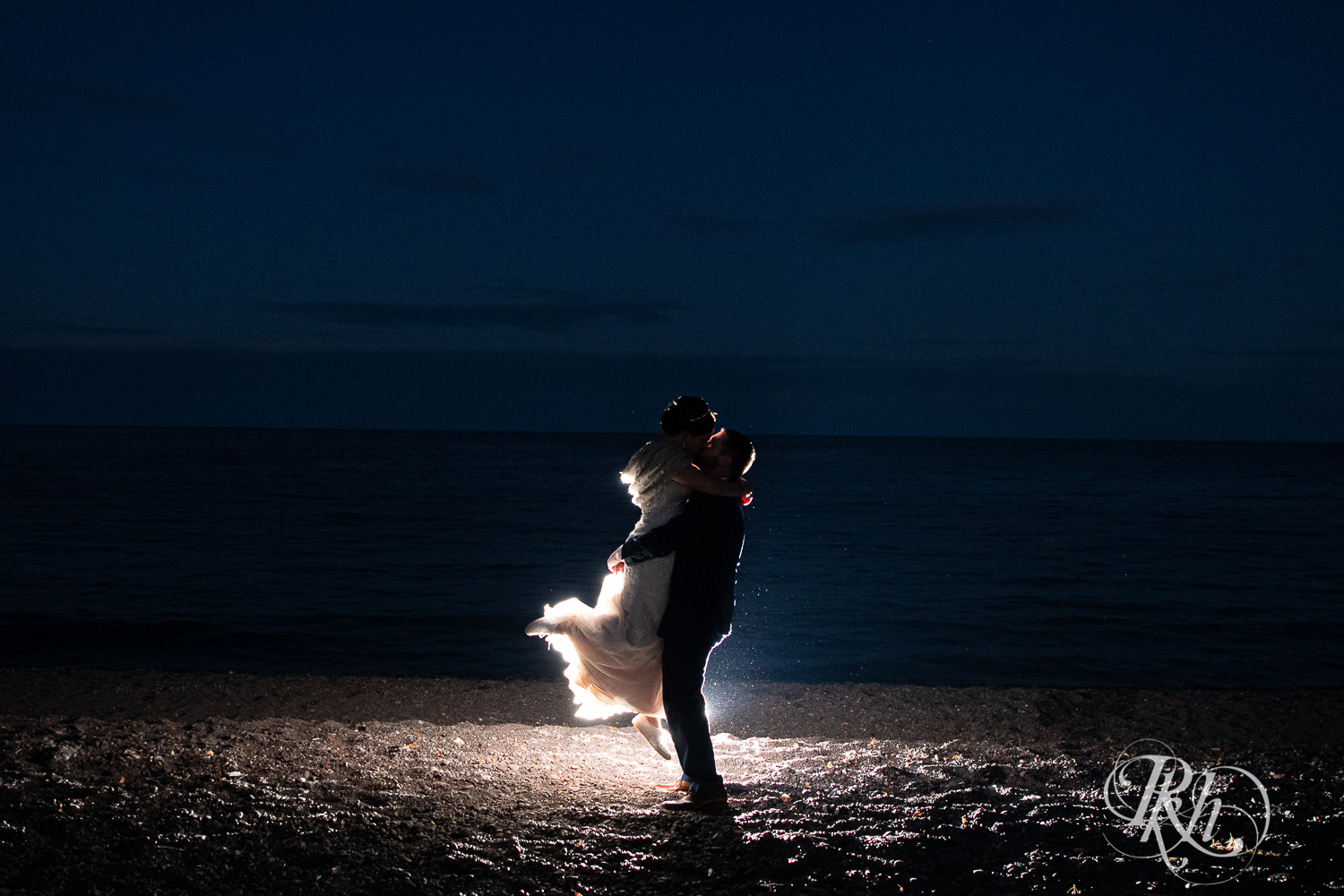 Groom lifts and kisses bride on beach at night at Superior Shores Resort in Two Harbors, Minnesota.