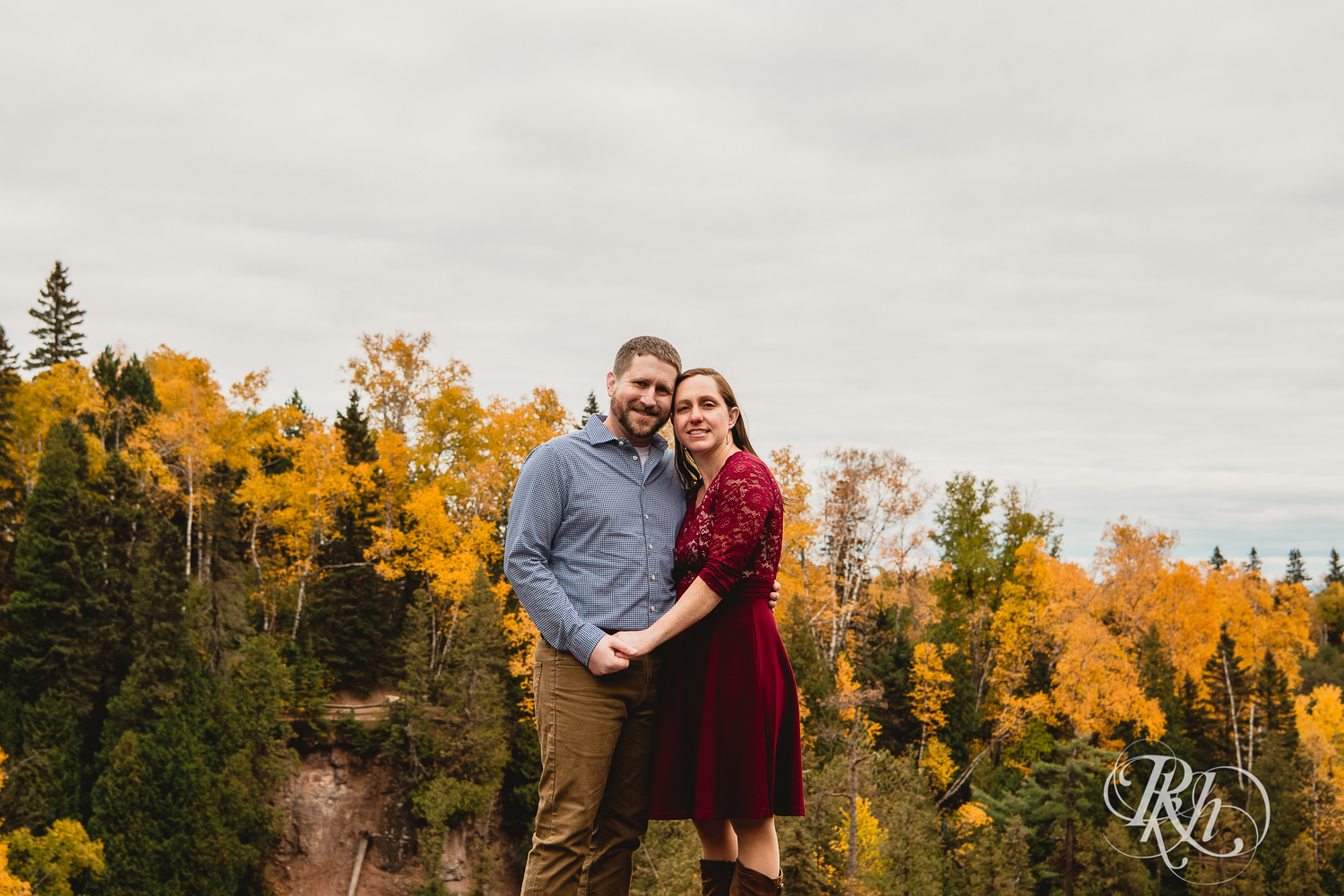 Man and woman in red dress smile in front of the fall colors in Gooseberry Falls in Two Harbors, Minnesota.