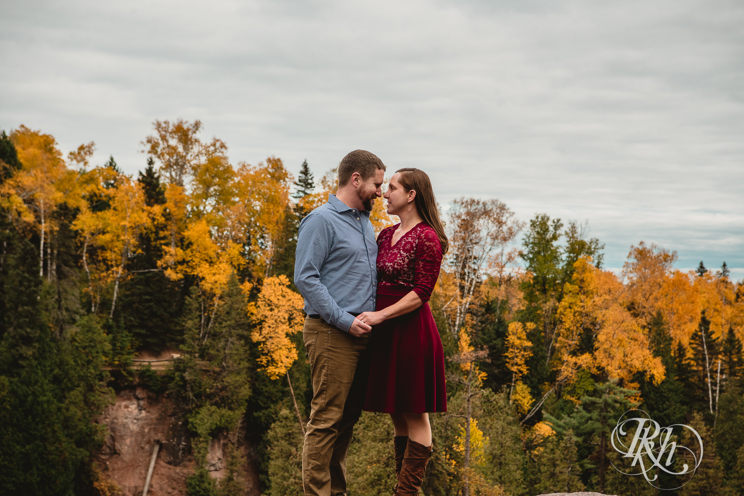 Man and woman in red dress smile in front of the fall colors in Gooseberry Falls in Two Harbors, Minnesota.