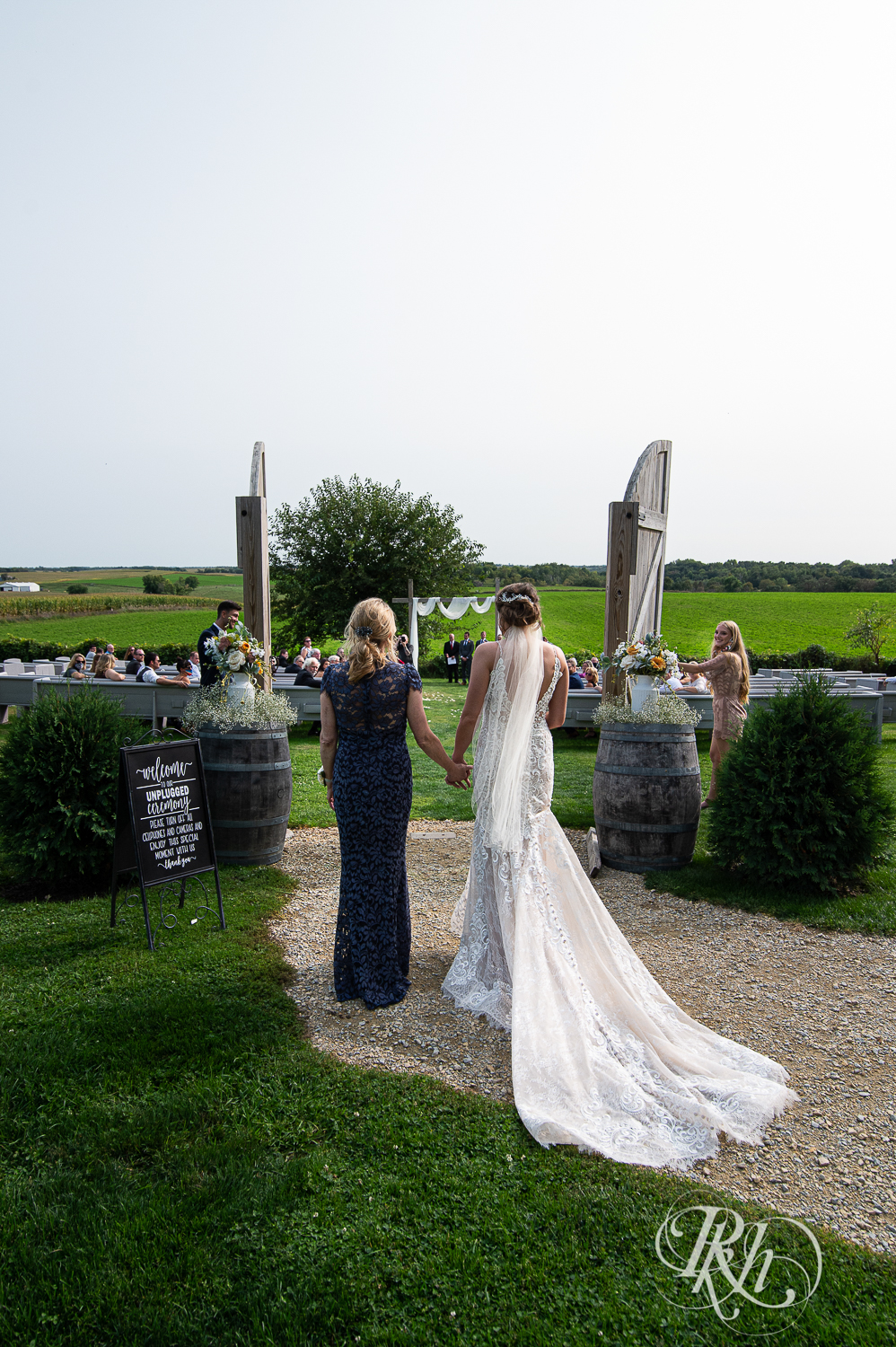 Bride walks down the aisle with mom during wedding ceremony at Legacy Hills Farm in Welch, Minnesota.