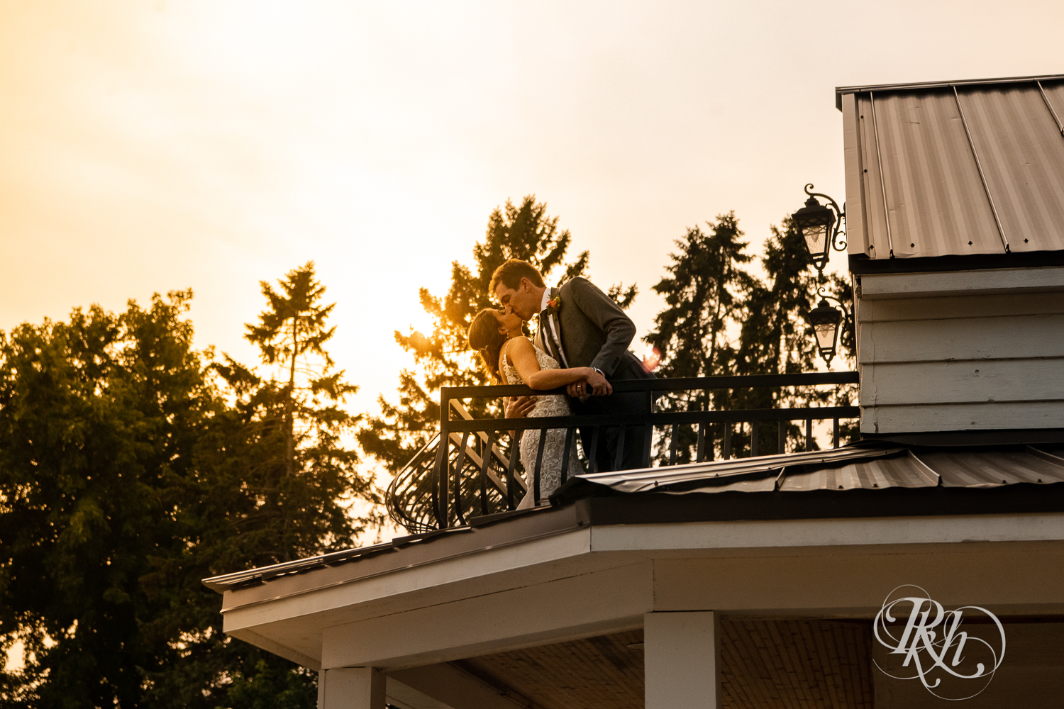Bride and groom kiss on balcony at sunset at wedding reception at Legacy Hills Farm in Welch, Minnesota.