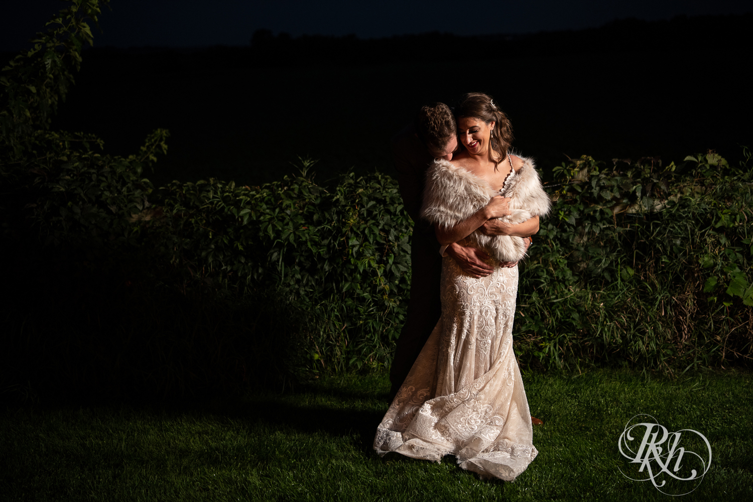 Bride smiles in fur stole and dress at night at Legacy Hills Farm in Welch, Minnesota.
