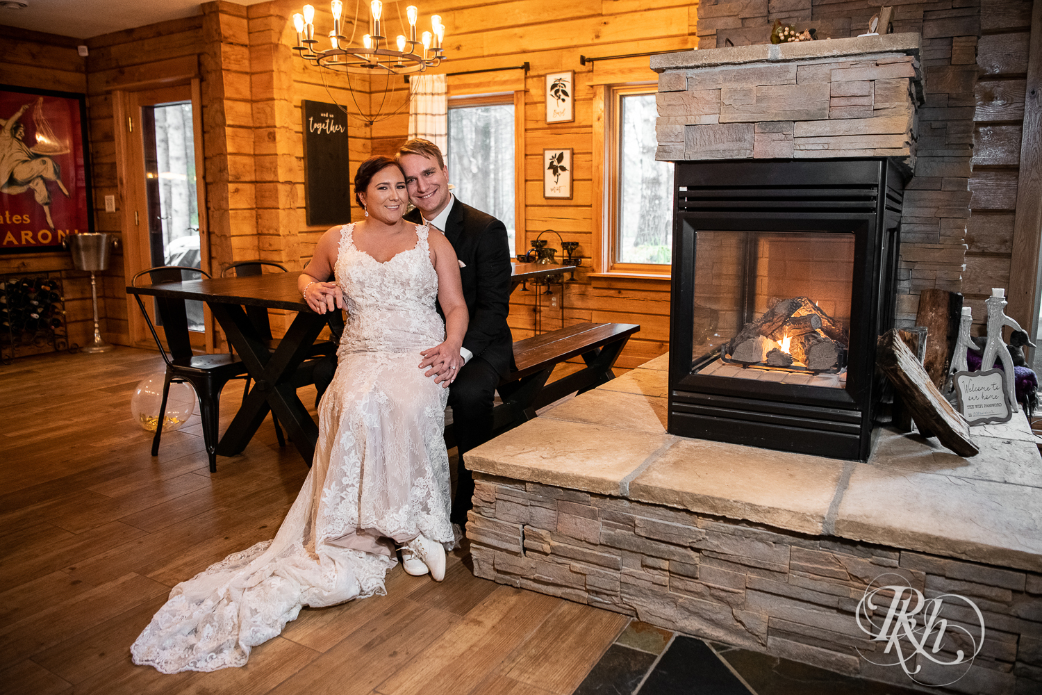 Bride and groom smile by the fireplace at a cabin A-frame in Stillwater, Minnesota.