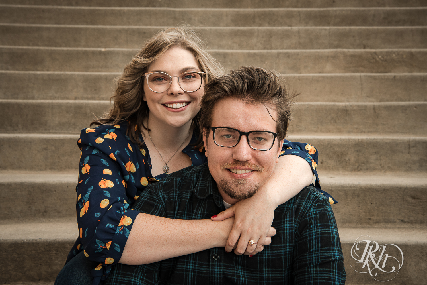 Blond woman with glasses and man with glasses smile on steps in Saint Paul, Minnesota.