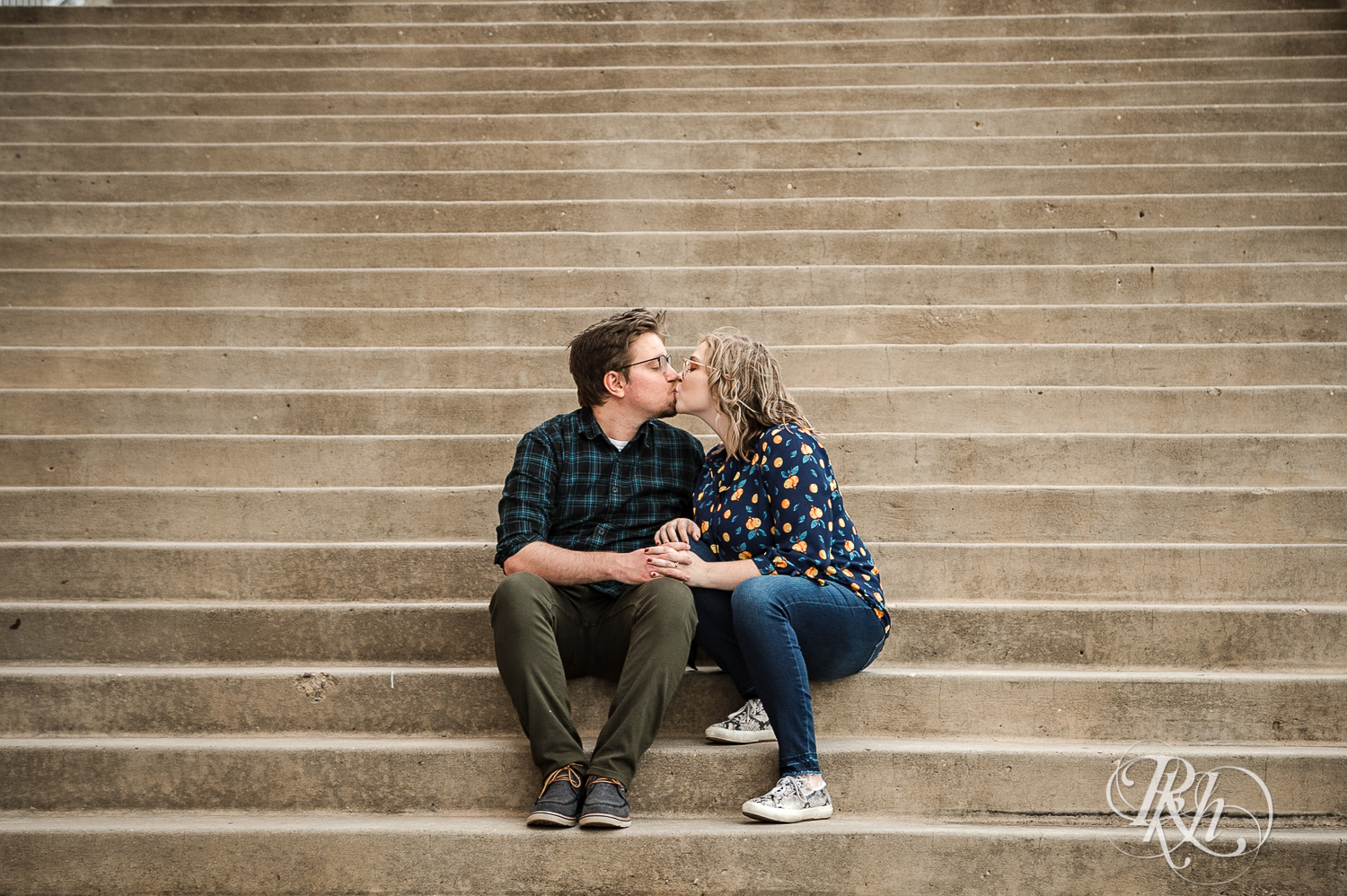 Blond woman with glasses and man with glasses kiss on steps in Saint Paul, Minnesota.