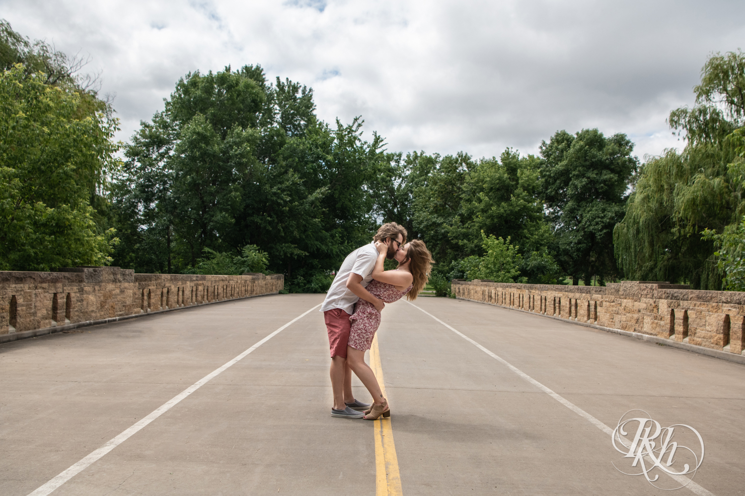 Man and woman kiss on bridge on cloudy day in Lake Phalen in Saint Paul, Minnesota.