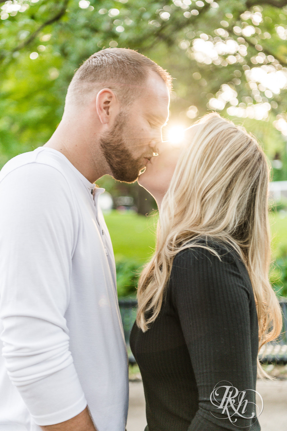 Blonde man and woman in sweaters and jeans kiss at sunset in Irvine Park in Saint Paul, Minnesota.