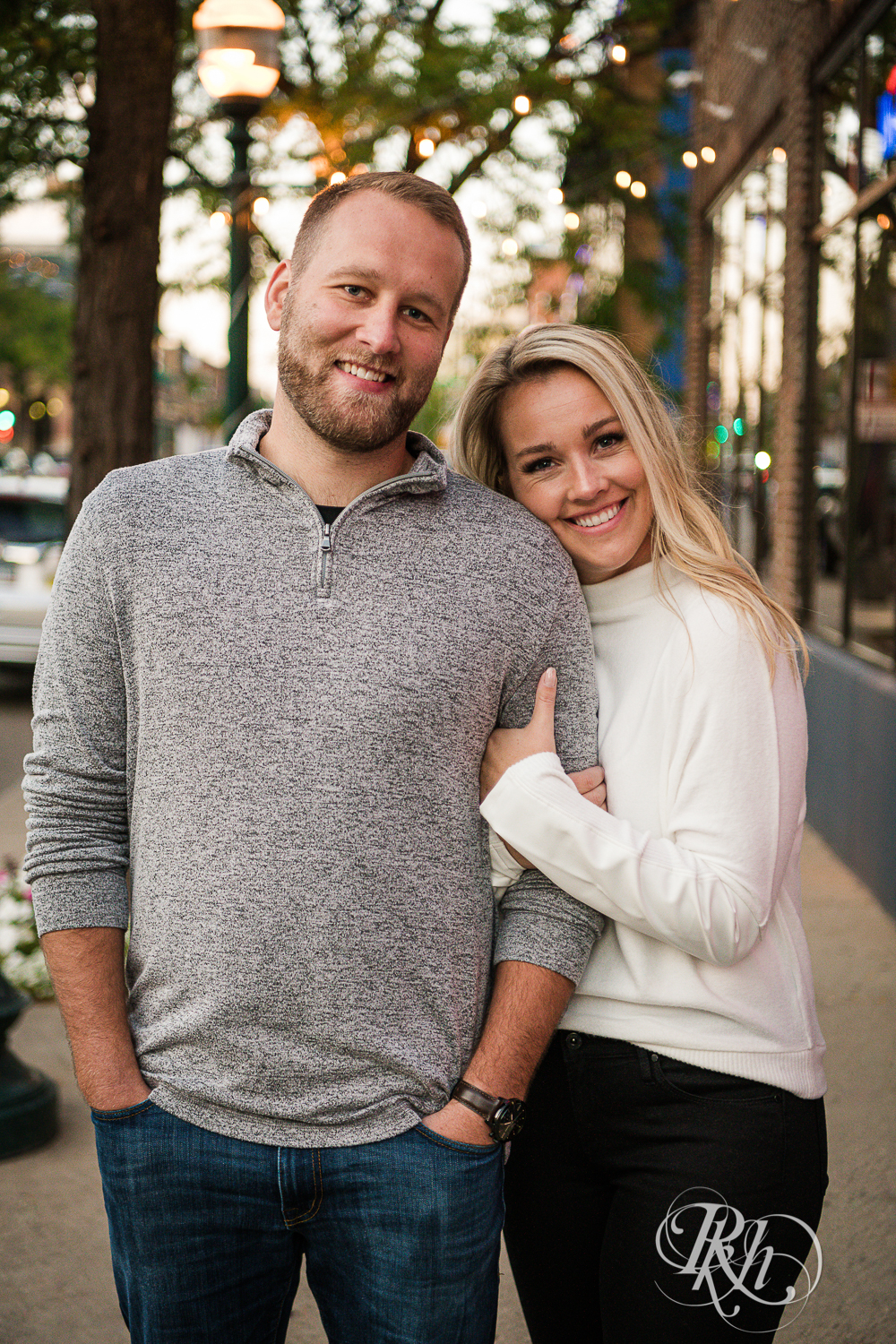 Blonde man and woman in sweaters and jeans smile at sunset in Saint Paul, Minnesota.