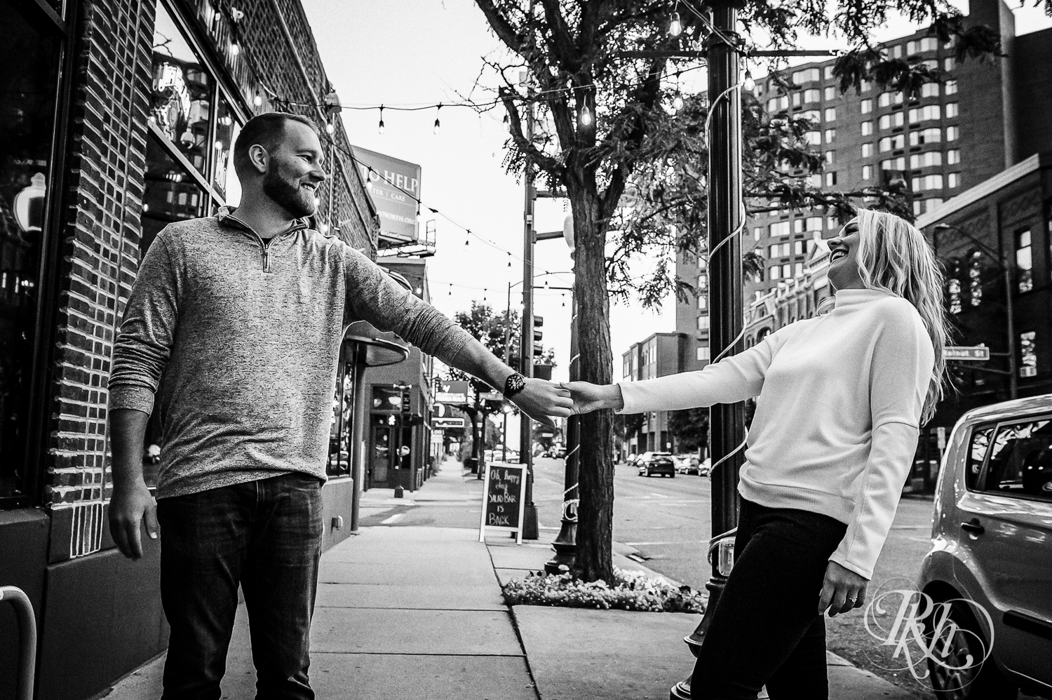 Blonde man and woman in sweaters and jeans dance on city sidewalk at sunset in Saint Paul, Minnesota.