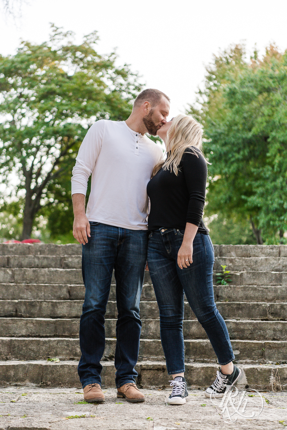 Blonde man and woman in sweaters and jeans kiss on stairs at sunset in Irvine Park in Saint Paul, Minnesota.