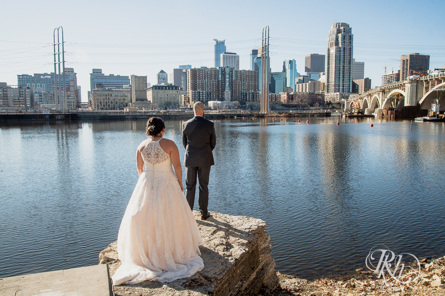 Bride and groom share first look at in front of river in Saint Anthony Main in Minneapolis, Minnesota.