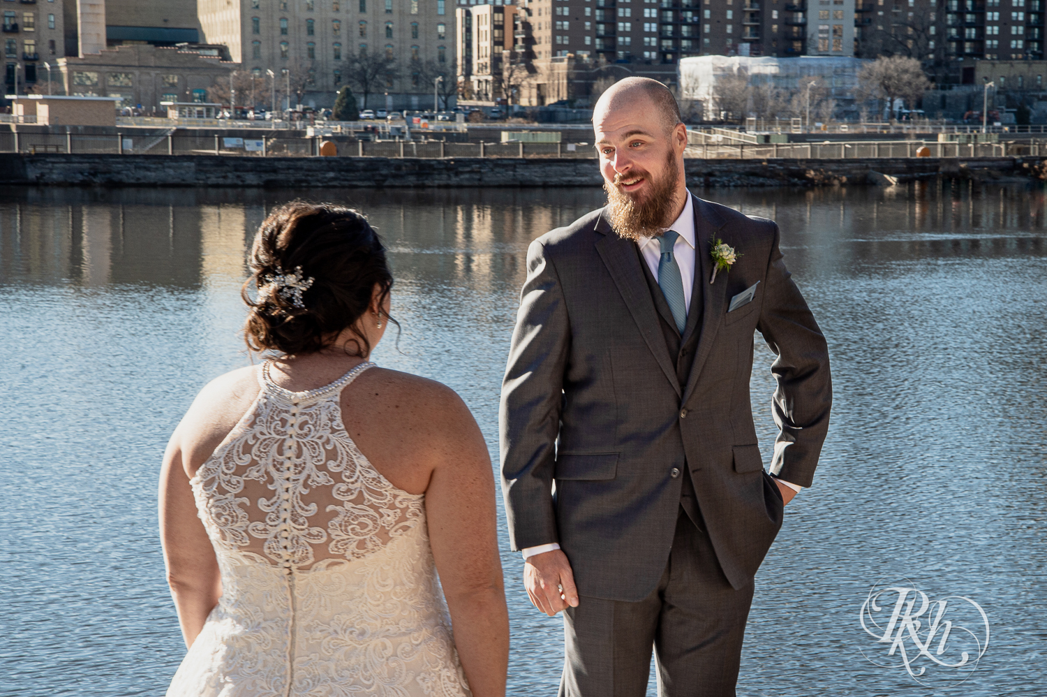 Bride and groom share first look at in front over river in Saint Anthony Main in Minneapolis, Minnesota.